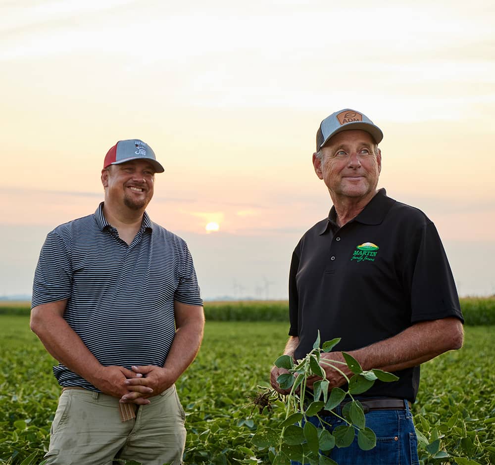 two producers standing in a soybean field smiling at something in the distance