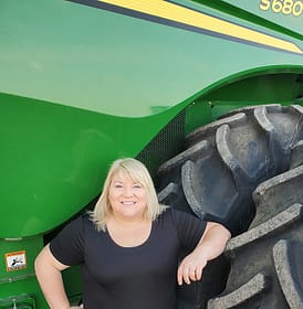 blonde woman leaning against a tractor wheel