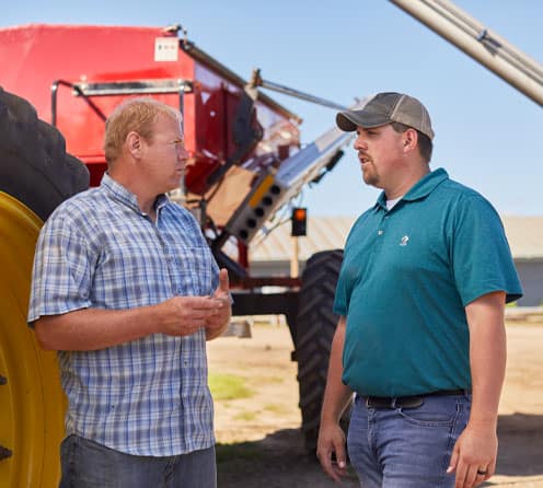 ADM representative talking with farmer next to fertilizer spreader
