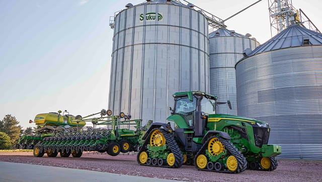 Green tractor parked in front of large silohs