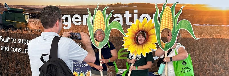 man taking a photo of three women posing with corn and flower cutouts