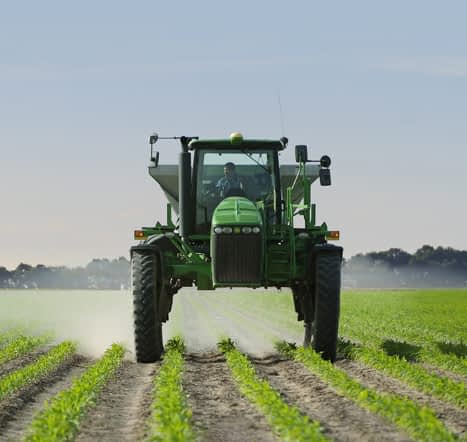 Tractor spreading fertilizer on young corn crop field